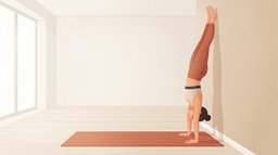 Eine Frau macht einen Handstand mit dem Rücken zu einer Wohnzimmerwand, die Arme gestreckt, der Körper kopfüber in einer Linie und die Fersen leicht an der Wand über einer terrakottafarbenen Matte